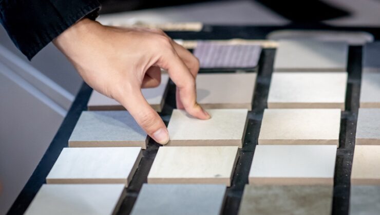 Male architect or interior designer hand choosing ceramic texture sample from swatch board in design studio. Floor and wall finishing material for architecture and construction industry.